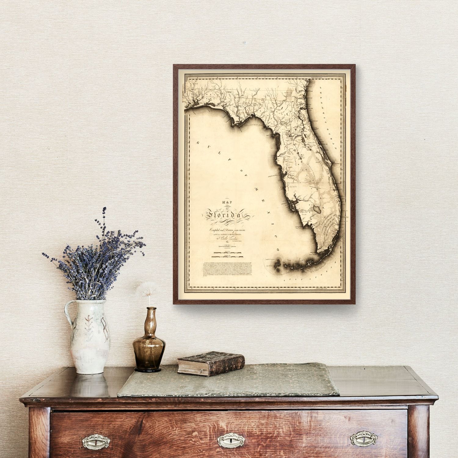 Framed vintage-style map of Florida on a white wall above a wooden dresser with decorative items.