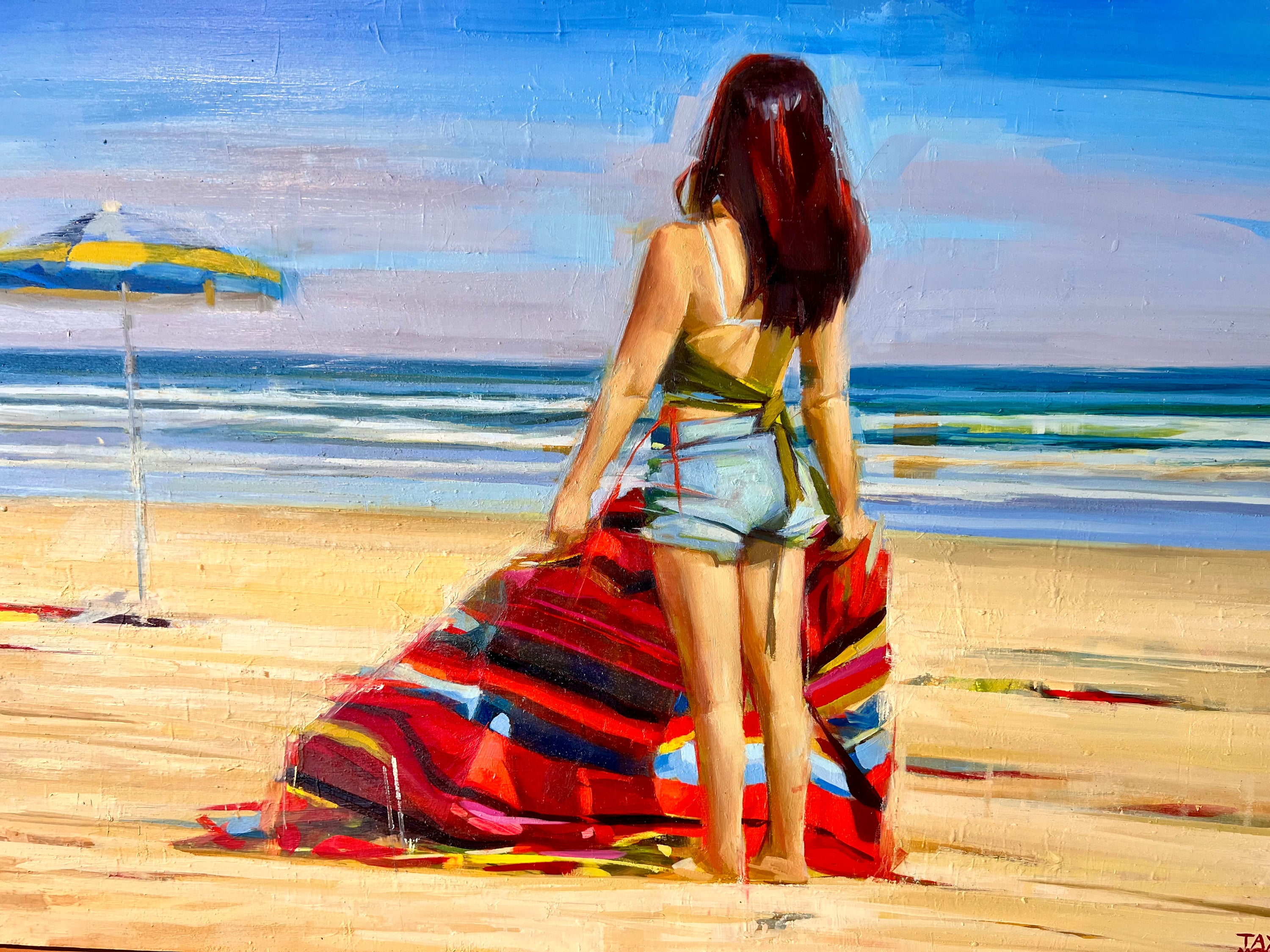 A colorful beach painting showing a woman from behind with red and black hair on a sandy shore, holding a striped red, blue, and black towel near the ocean with a blue sky and beach umbrella in the background. She's wearing a yellow tank top and light blue denim shorts.