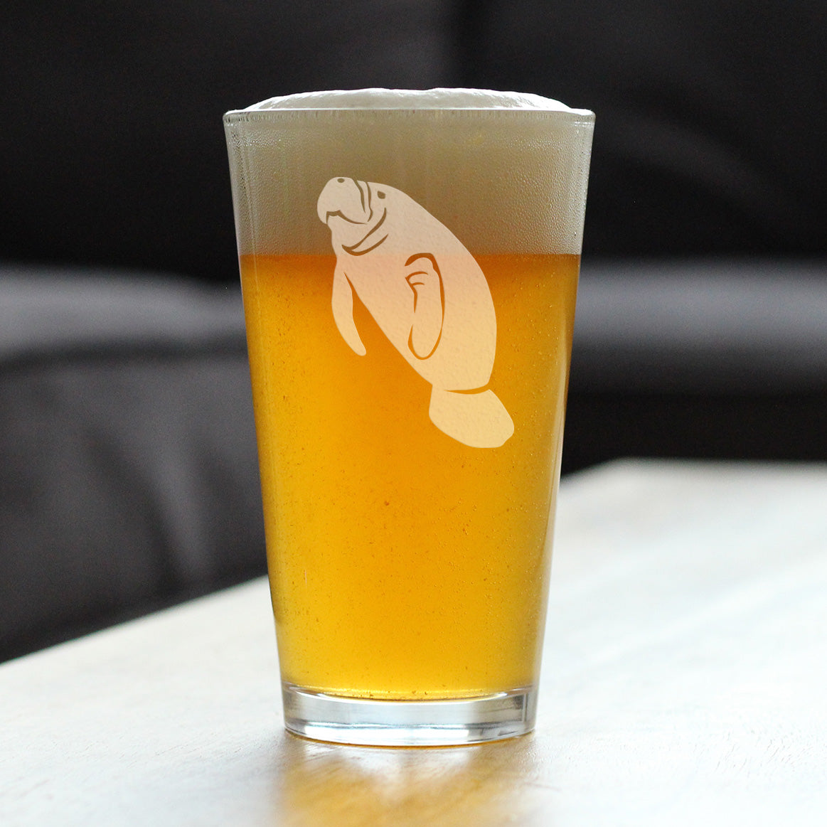 Clear glass with a manatee etching on it, filled with beer and sitting on a wooden table.